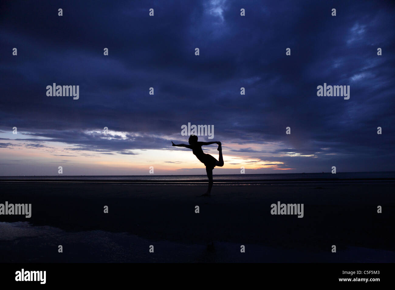 A woman practices yoga postures at dawn, Pranburi beach. Stock Photo