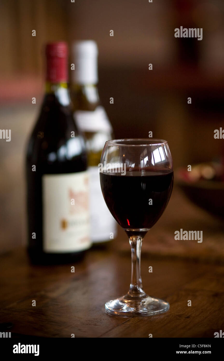 A glass of red wine on a table in front of two wine bottles Stock Photo