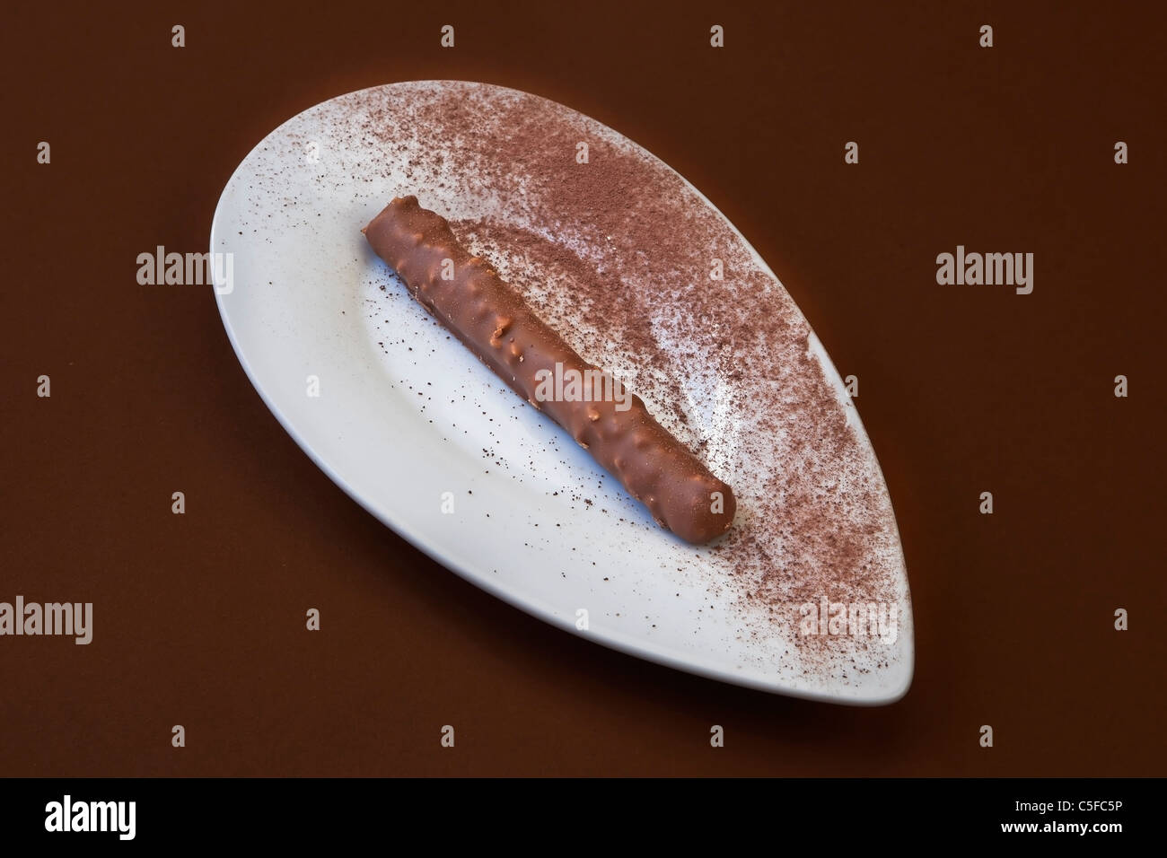 a long chocolate praline on a white plate with cocoa powder Stock Photo