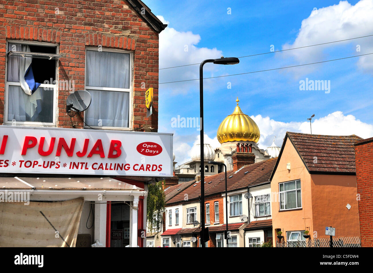 Golden dome of Sikh temple looming over the roofs of residential houses in Southall with a corner shop in foreground West London England UK Stock Photo