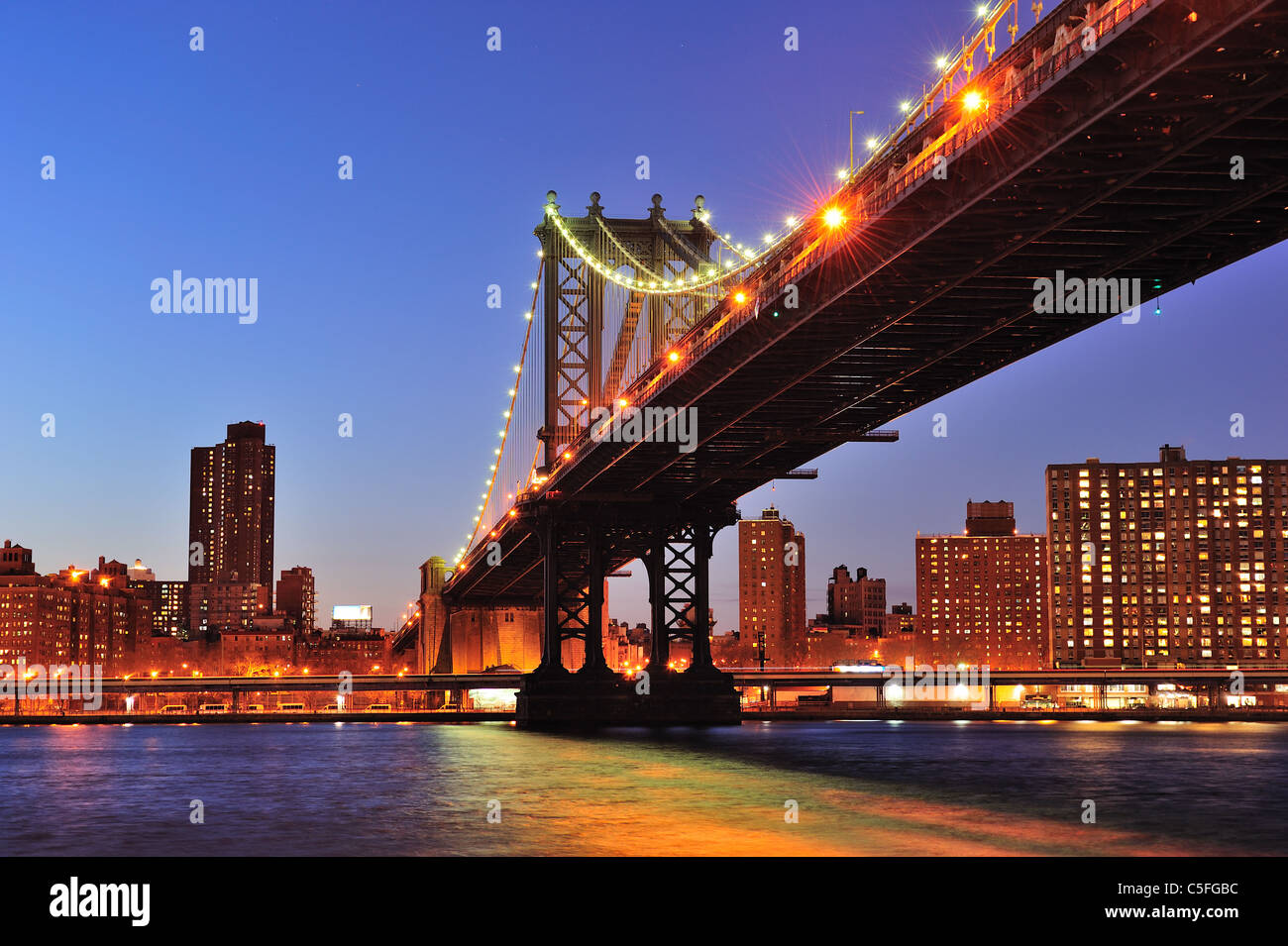 New York City Manhattan Bridge over East River at dusk illuminated with light with reflections and downtown skyline Stock Photo