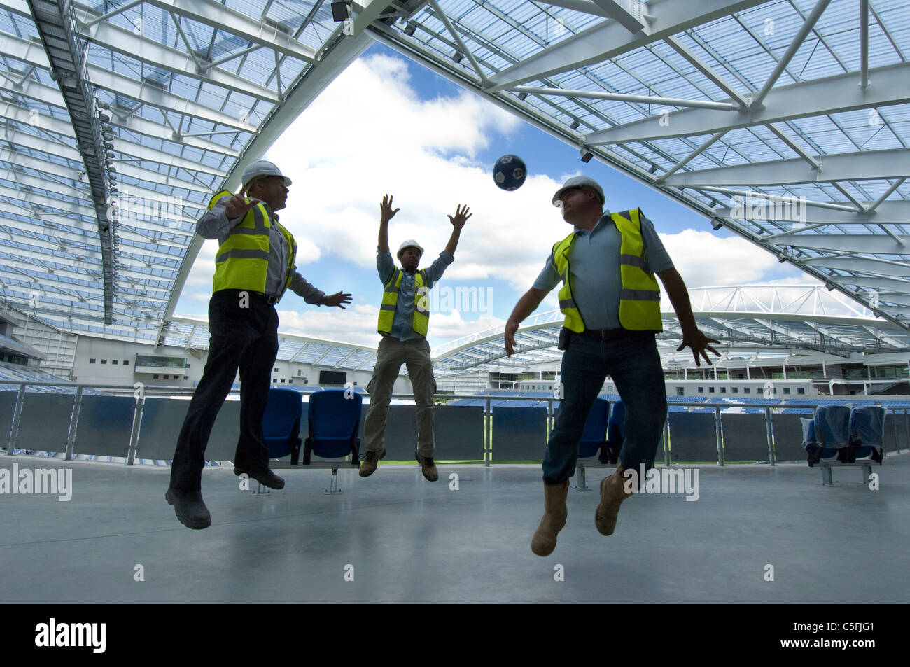 Three builders having a kickabout as work nears completion on the new AMEX stadium, home of Brighton and Hove Albion from 2011. Stock Photo