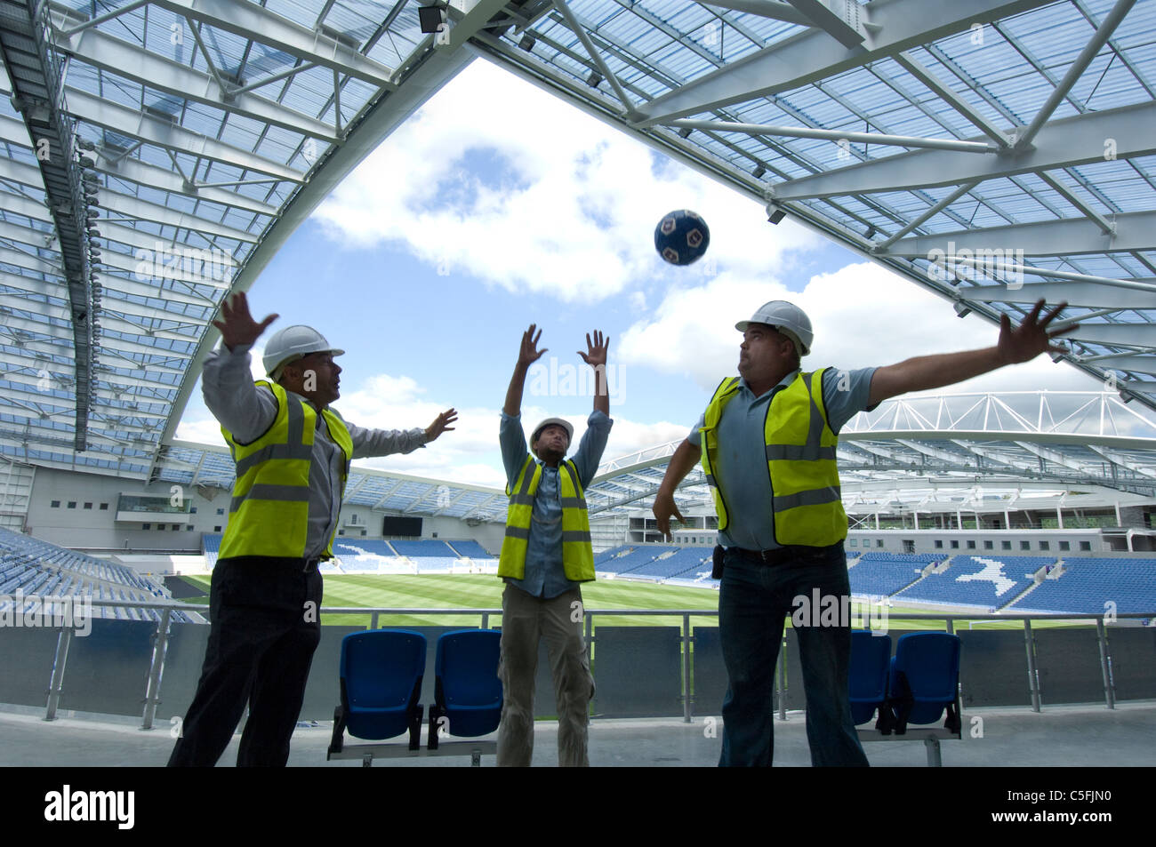 Three builders having a kickabout as work nears completion on the new AMEX stadium, home of Brighton and Hove Albion from 2011. Stock Photo