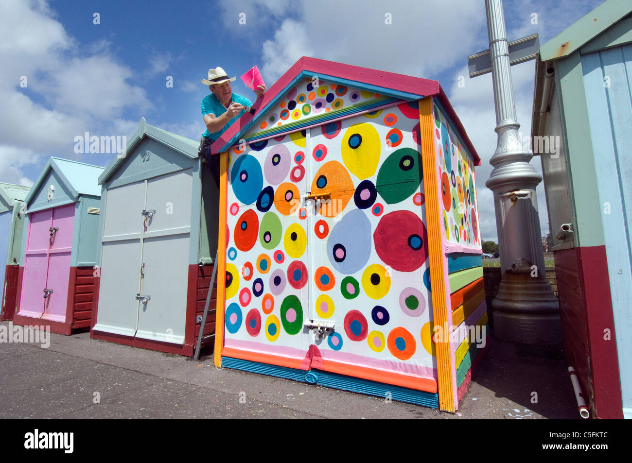 A middle aged man defying he rules and painting his Brighton beach hut in non-regulation colourful spots. Stock Photo