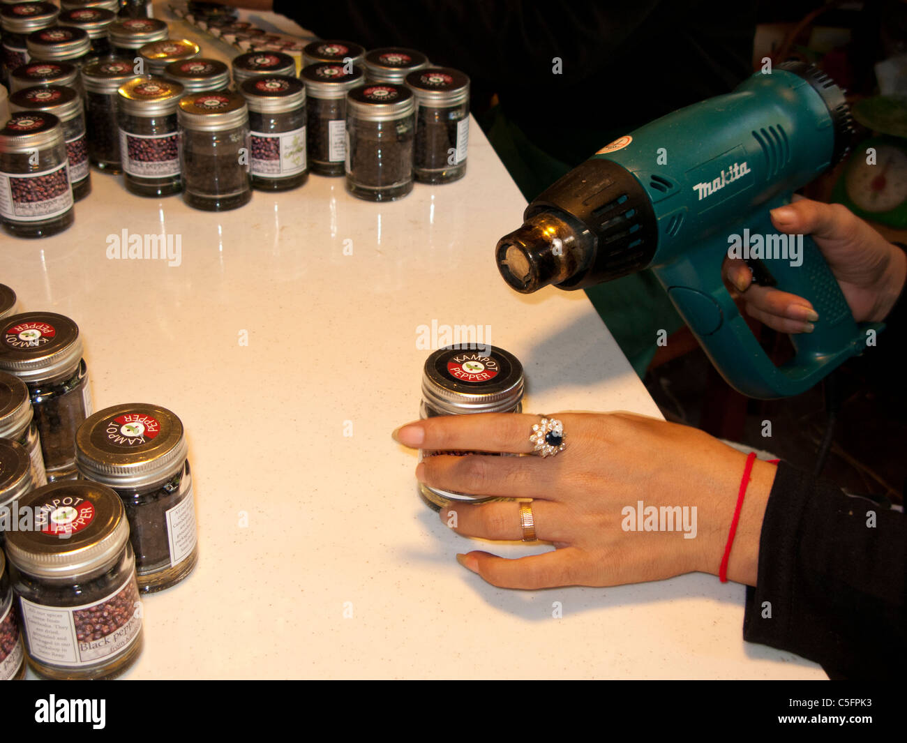 Worker heat sealing the lid on a jar of Kampot black pepper at the