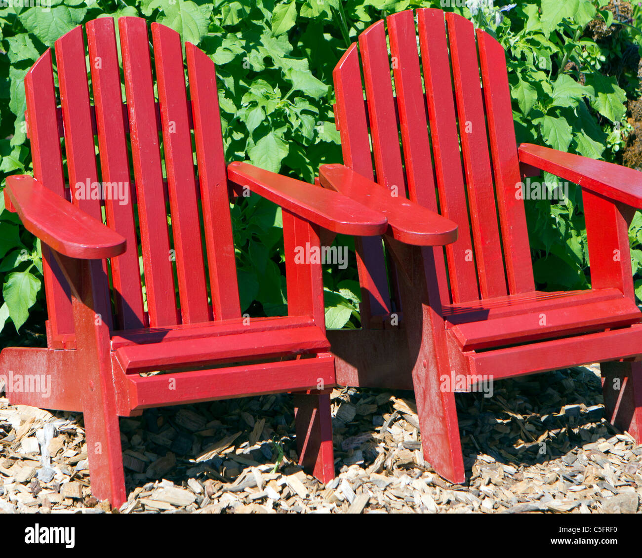 Two red Adirondack chairs in a row sitting in a garden Stock Photo Alamy
