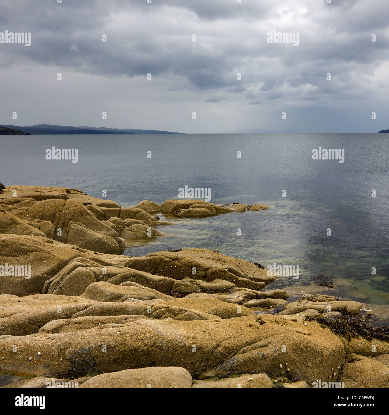 Rocky shoreline, calm sea loch with cloudy, threatening grey sky, Camas Malag, Torrin,Isle of Skye, Scotland, UK Stock Photo