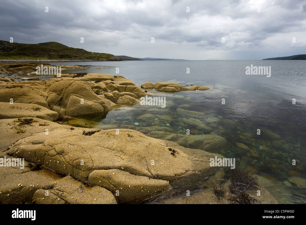 Rocky shoreline, calm sea loch with cloudy, threatening grey sky, Camas Malag, Torrin,Isle of Skye, Scotland, UK Stock Photo