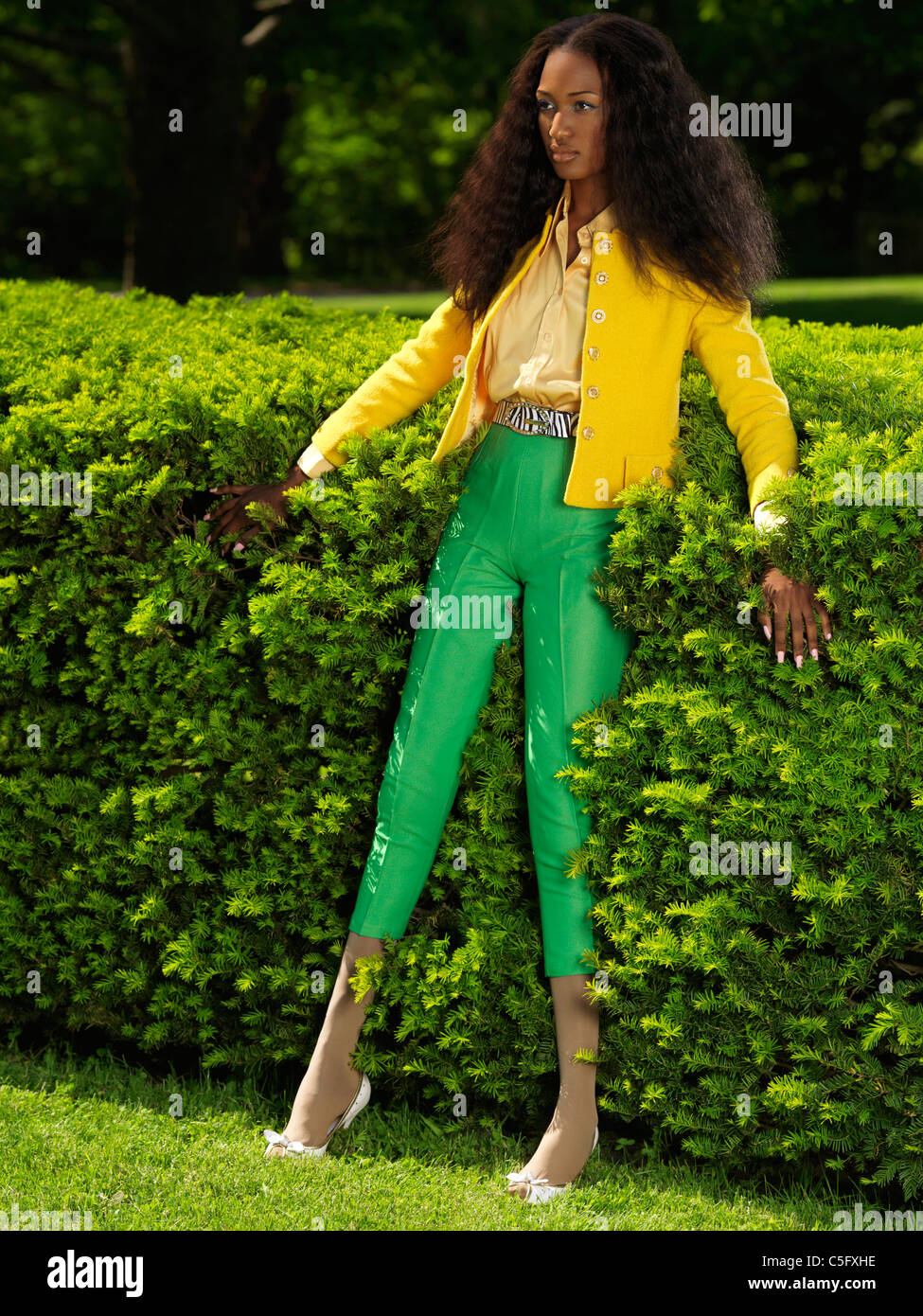 Young stylish black woman in fancy bright clothes leaning against green  bushes Stock Photo - Alamy