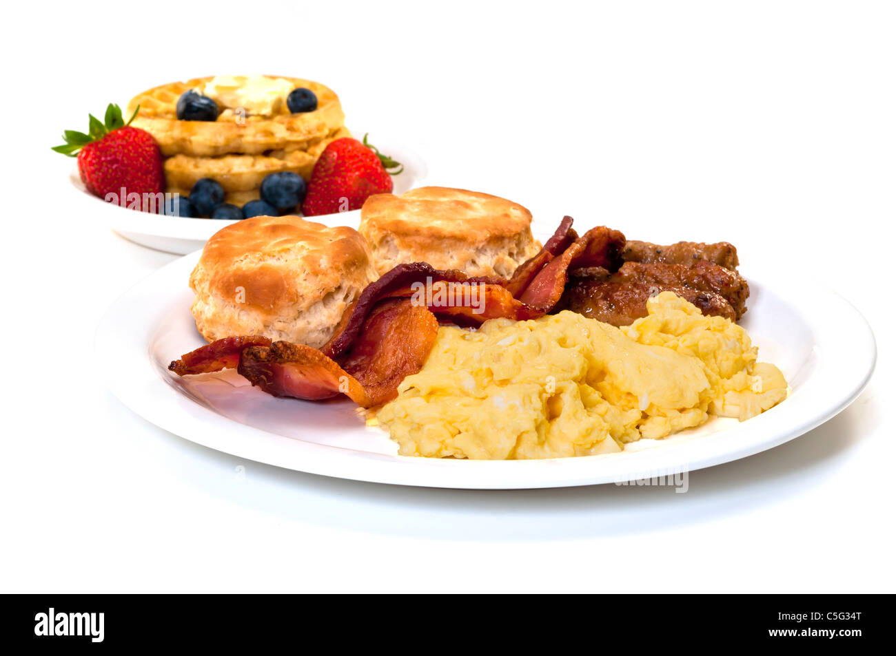 Scrambled eggs, bacon, link sausage, biscuits,  and waffles with strawberries and blueberries.  Isolated on white background. Stock Photo