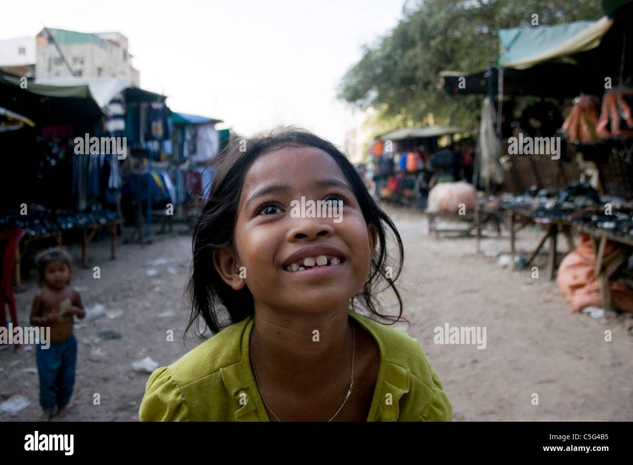 A young girl living in poverty is smiling near her home in a slum in Phnom Penh, Cambodia. Stock Photo