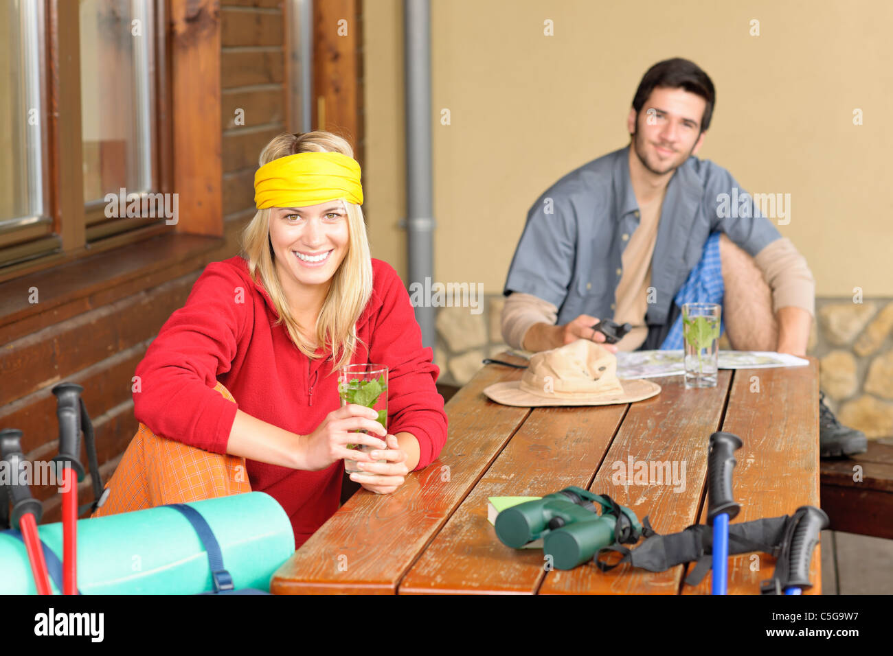 Tramping young couple backpack relax by wooden table drink water Stock