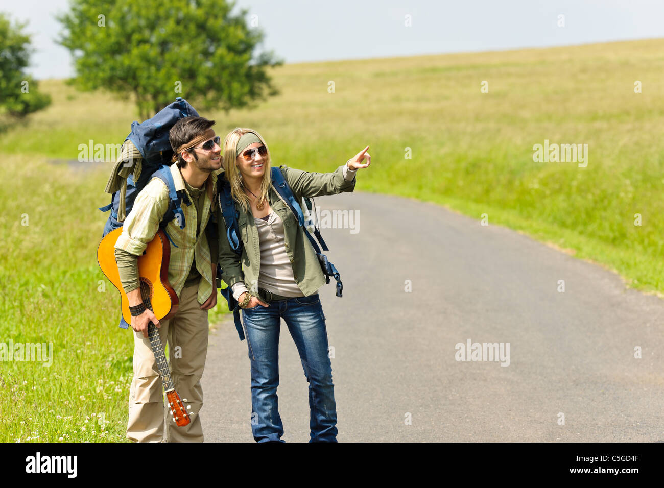 Hiking young couple backpack tramping on asphalt road sunny countryside Stock Photo