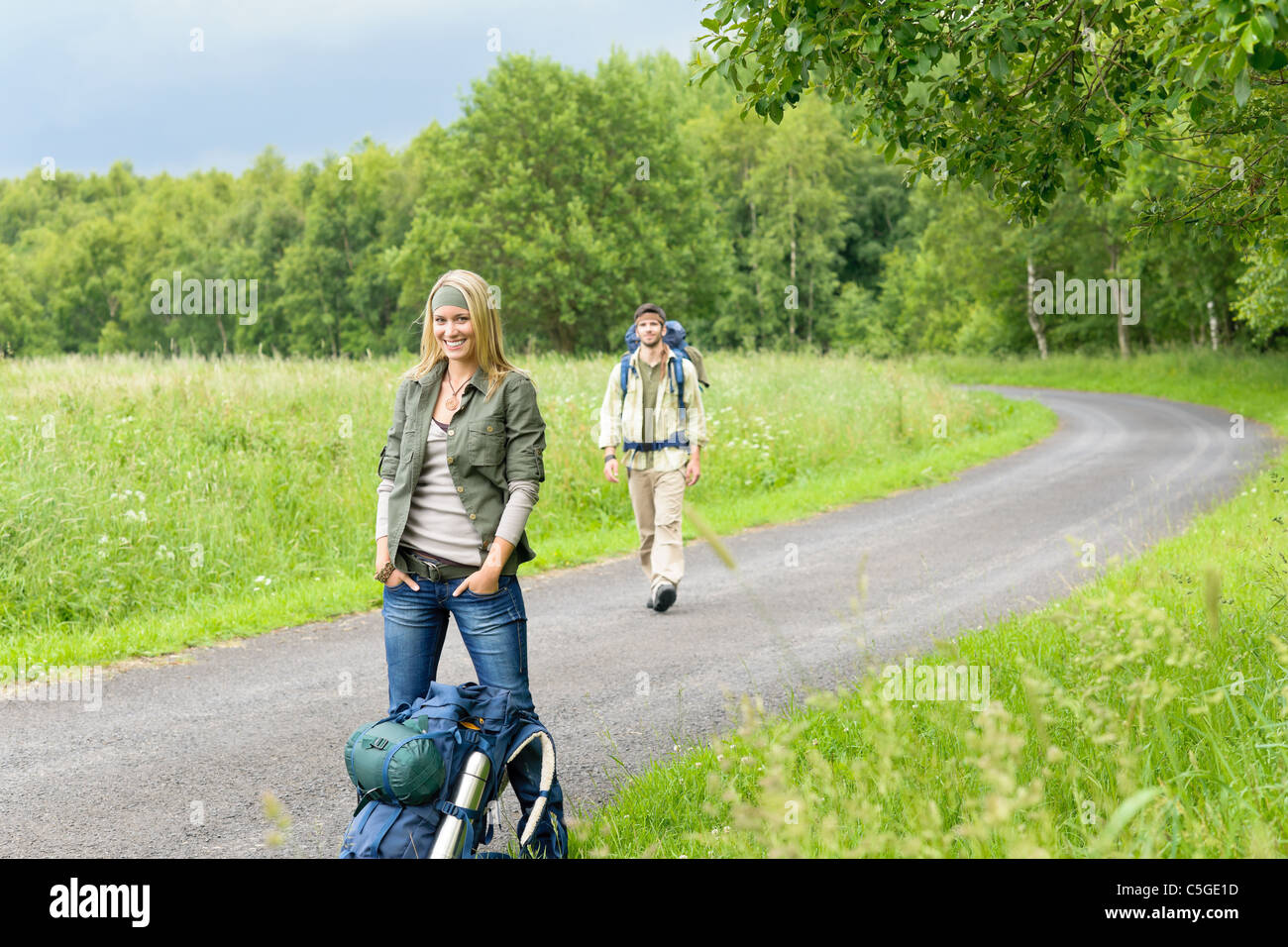 Hiking young couple backpack tramping on asphalt road countryside Stock