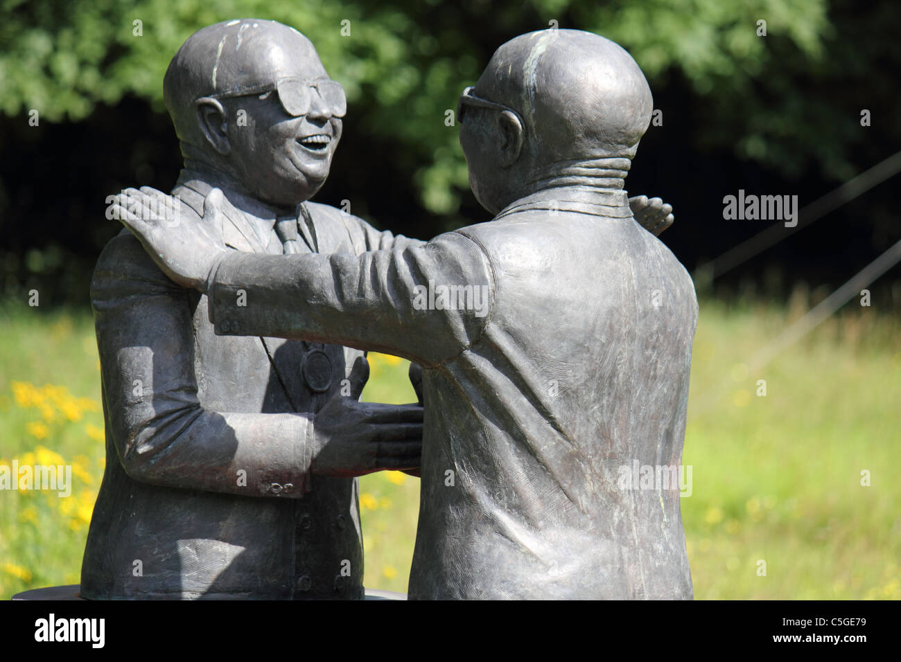 a statue of two bald men wearing sunglasses greeting each other, shaking hands and patting shoulders Stock Photo