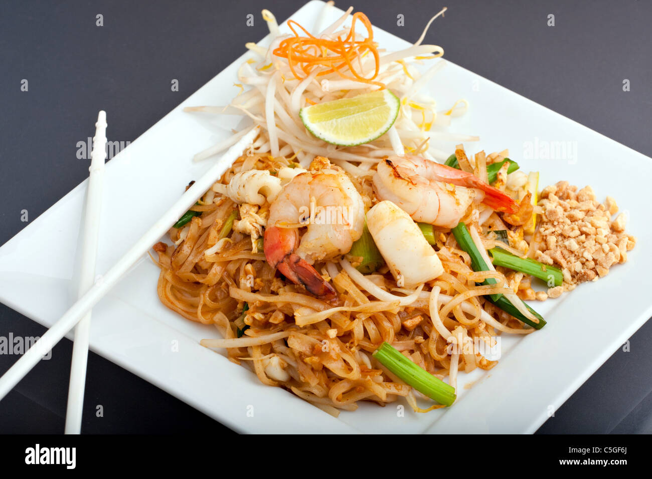 Seafood pad Thai dish of Thai fried rice noodles on a square white plate with chopsticks and grated carrot garnish. Stock Photo