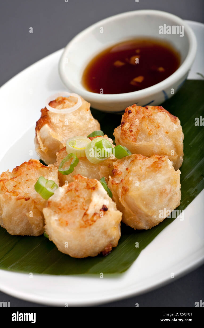 Fried thai appetizers with soy dipping sauce presented on a plate with banana leaf and scallion garnish. Stock Photo