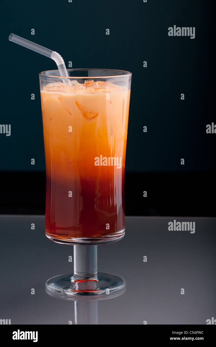 Thai iced tea served in a tall glass with cream and a straw. Stock Photo
