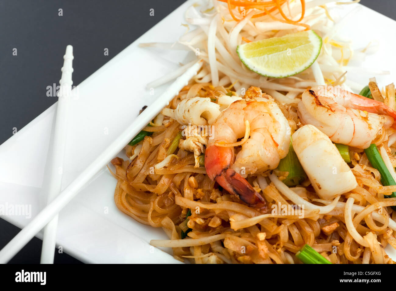 Seafood pad Thai dish of fried rice noodles on a square white plate with chopsticks and grated carrot garnish. Stock Photo