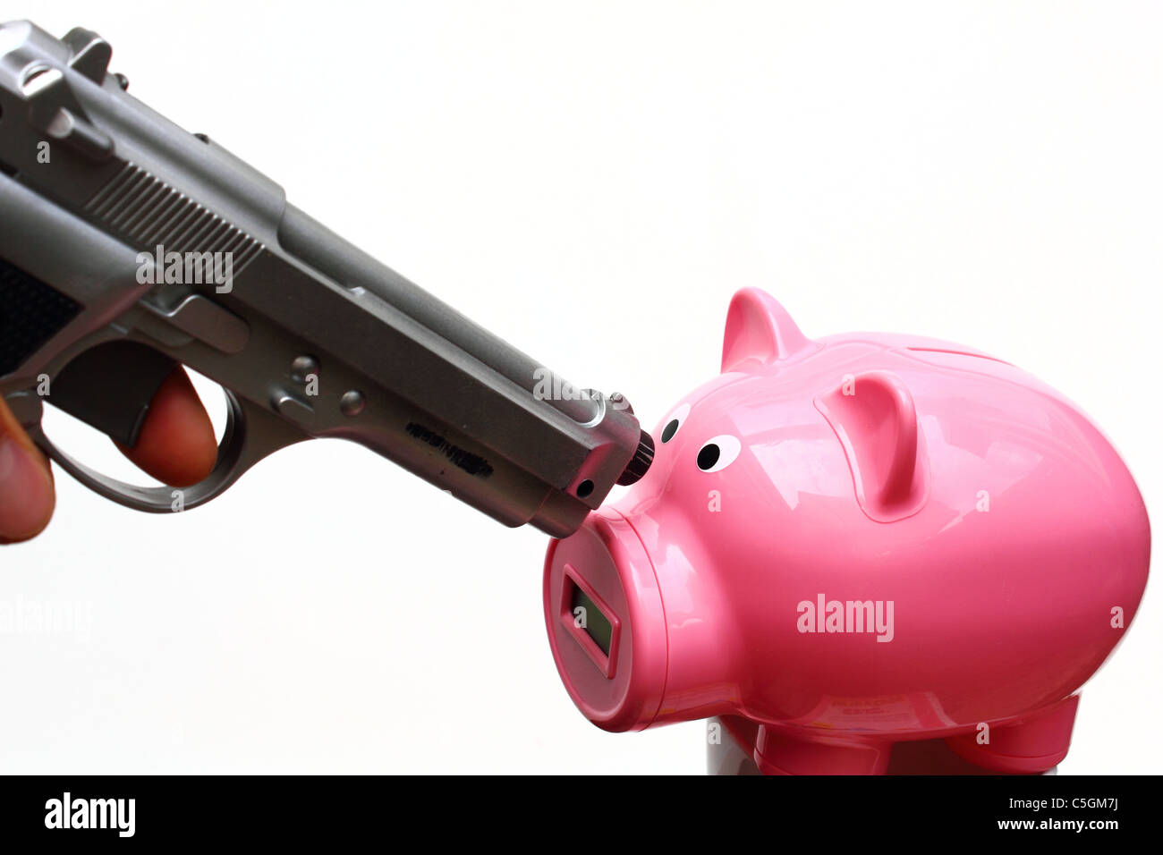 A silver colored gun is pointed towards a pink piggy bank. Stock Photo