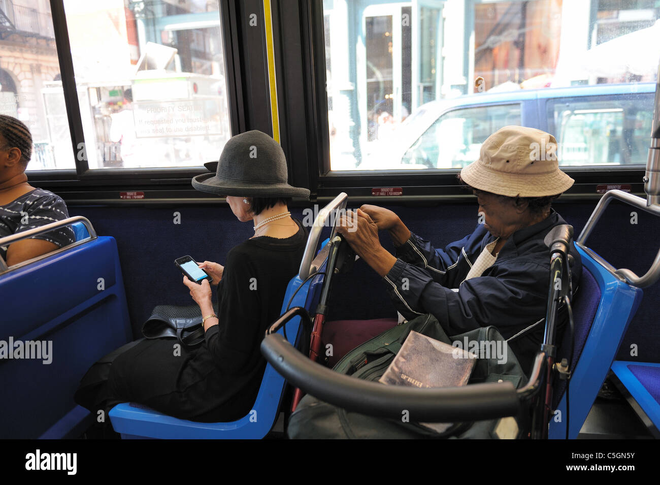 An expensively dressed woman and a poor one with a walker and a Bible sitting near each other on a Manhattan bus. July 20, 2011 Stock Photo