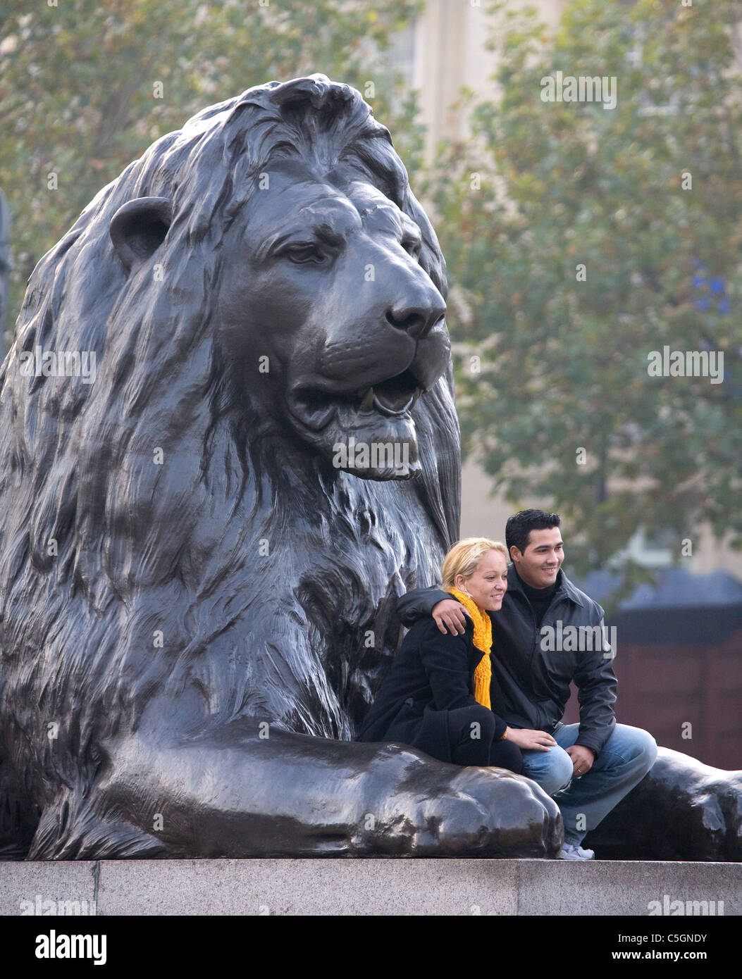 A young couple pose for a photograph in front of a Landseer lion in Trafalgar Square in London Stock Photo