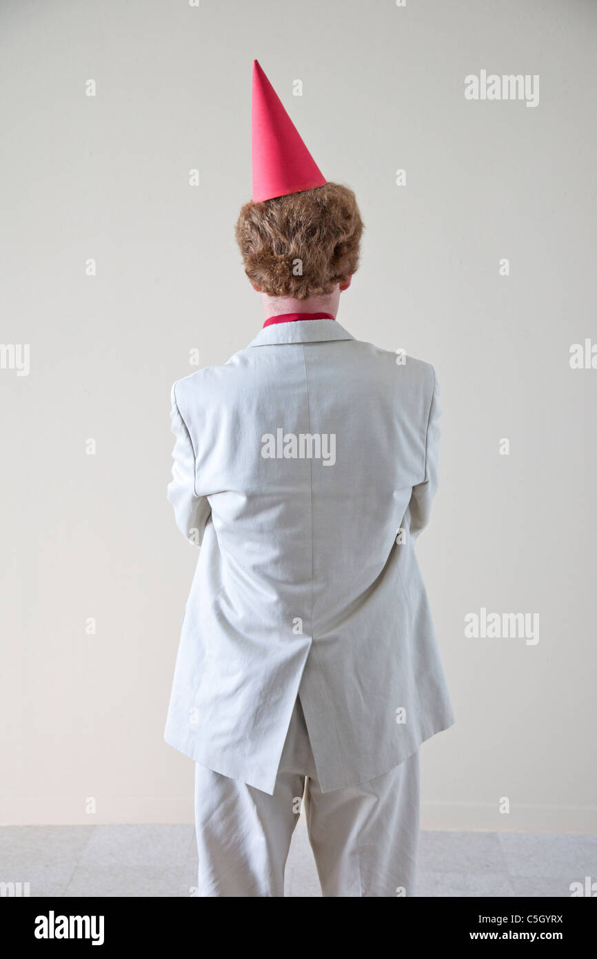 man with red dunce cap stands with back to us and folded arms Stock Photo Alamy