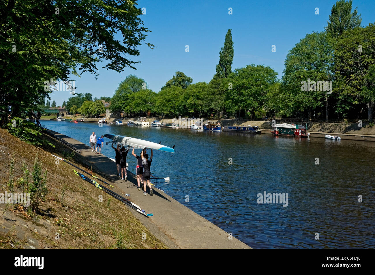 Young men man people carrying rowing boat next to River Ouse in summer York North Yorkshire England UK United Kingdom GB Great Britain Stock Photo