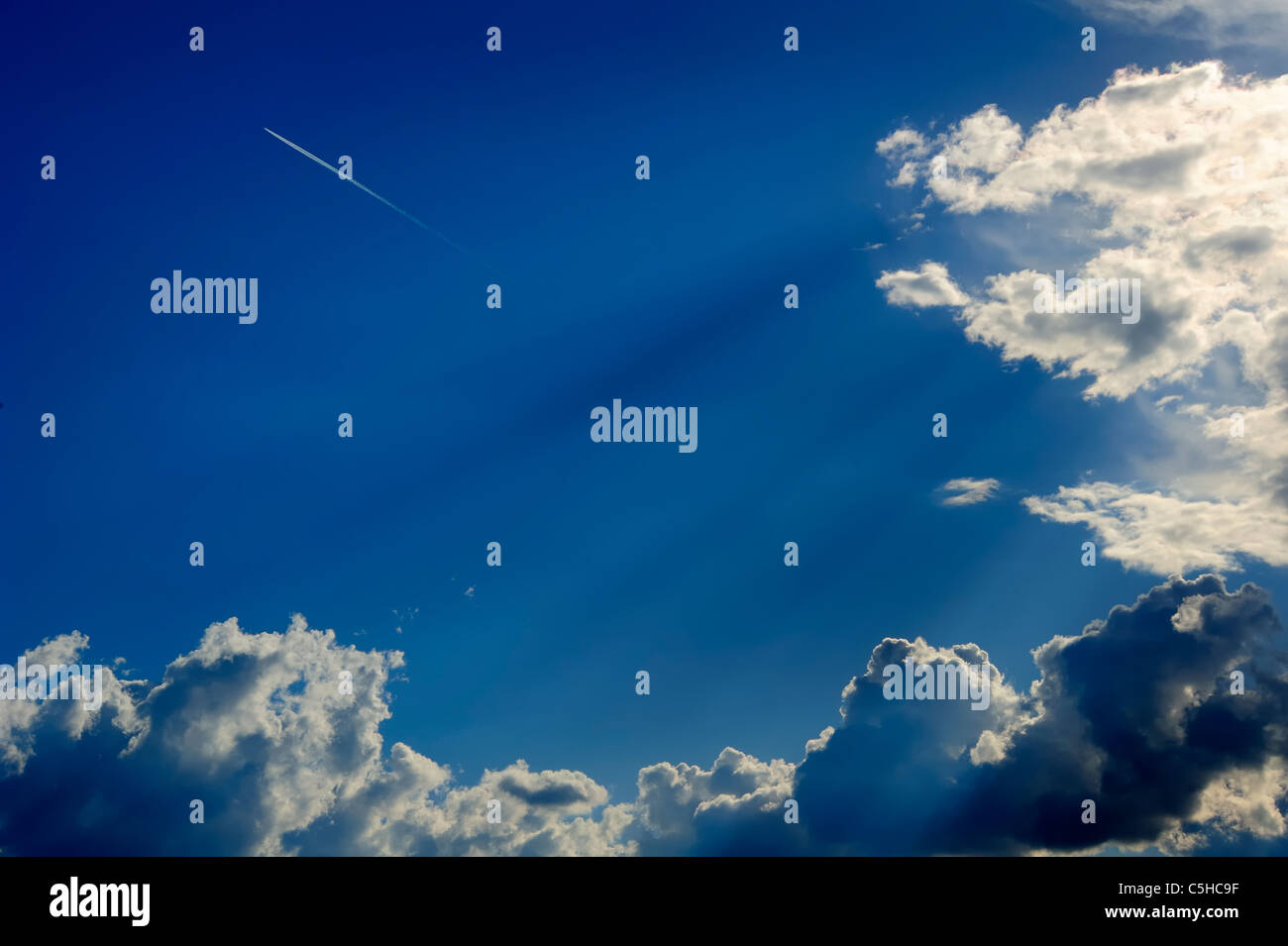 A jet airliner flying beyond a bank of cumulus clouds with crepuscular rays showing. Space for text in the sky. Stock Photo