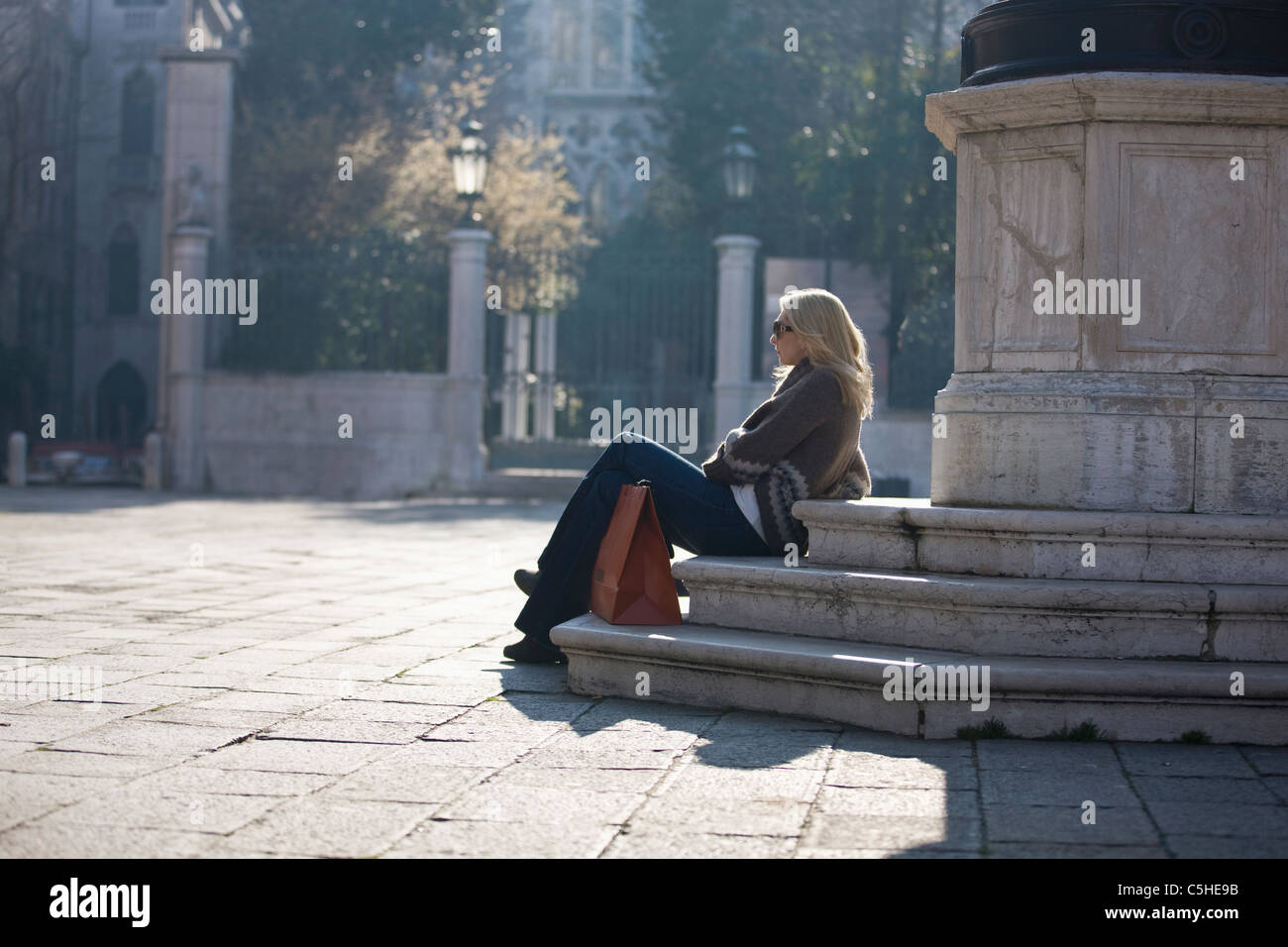 A woman sitting at the base of a statue, Campo Santo Stefano,Venice, Italy Stock Photo