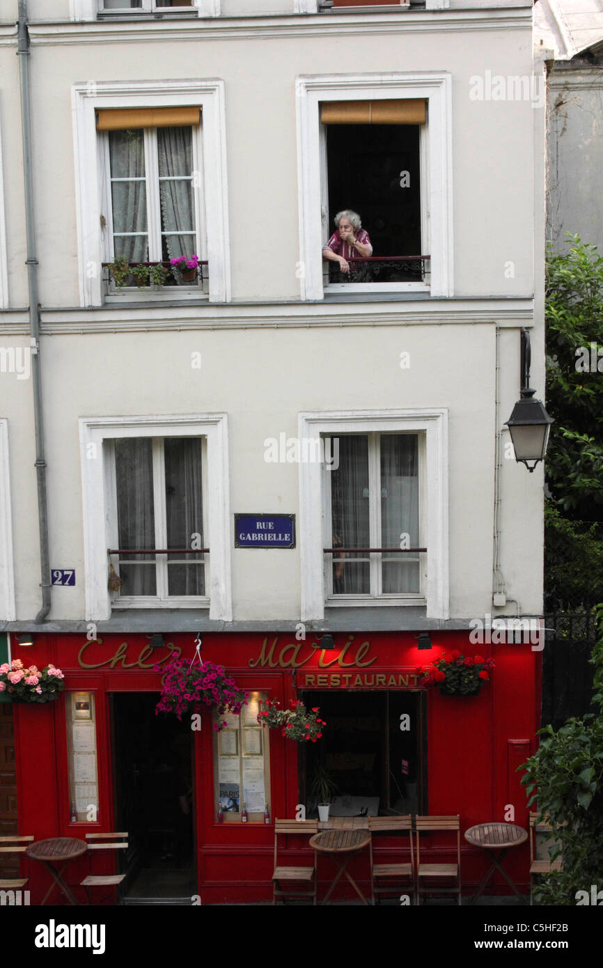 Old woman in a window above a restaurant in Paris Stock Photo