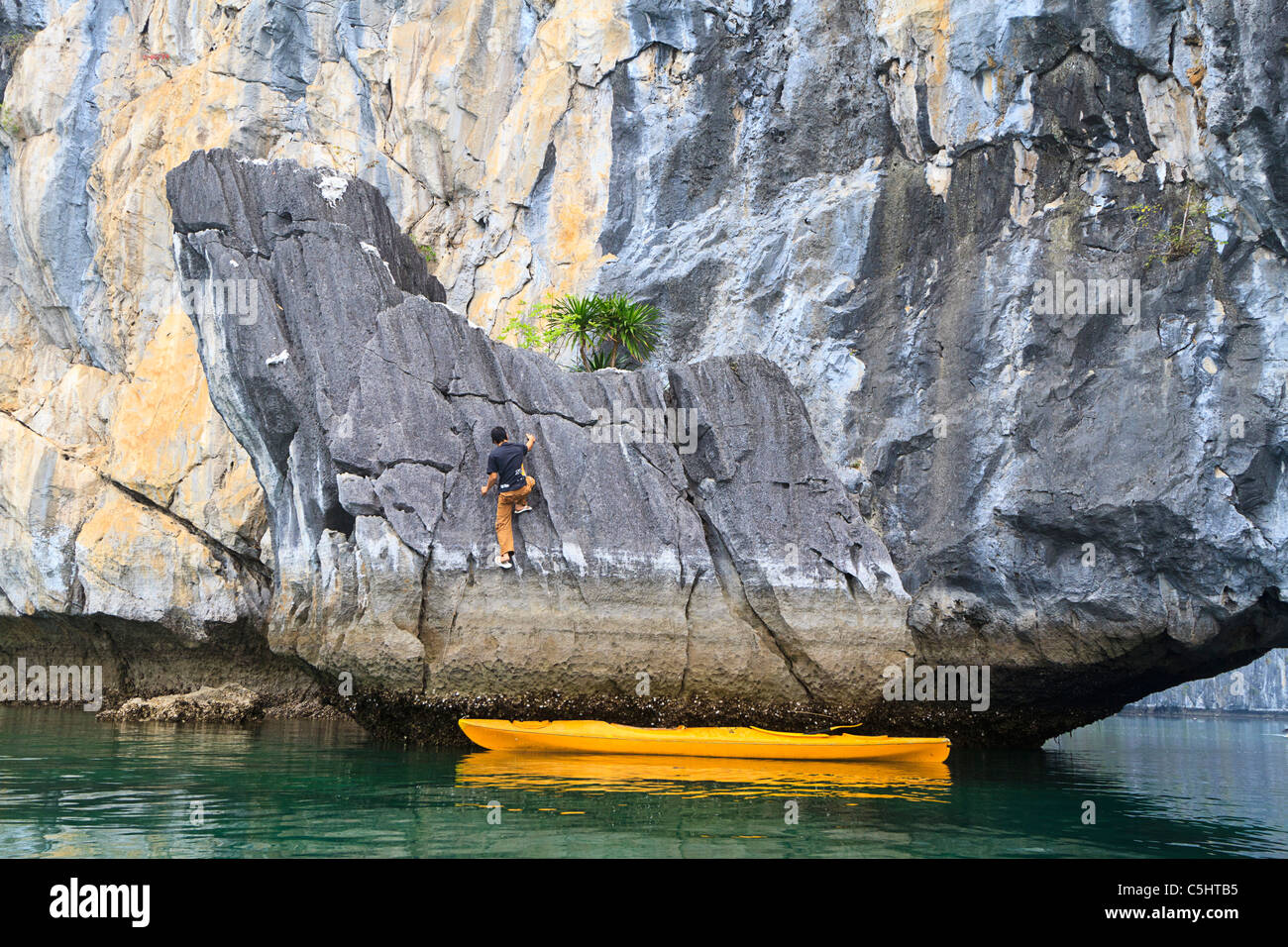 Young man climbs limestone rock wearing rubber flip flop sandals. He traveled to the rock via kayak. Stock Photo