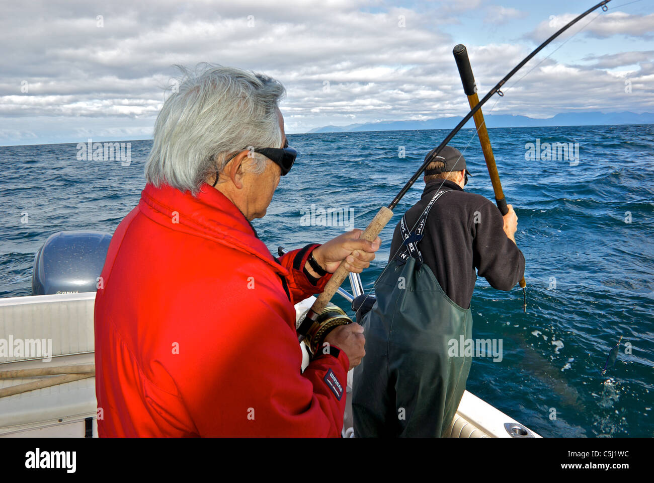 Sport fishing guide ready to harpoon big halibut for charter angler guest rough seas open Pacific Ocean Kyuquot Sound BC Stock Photo