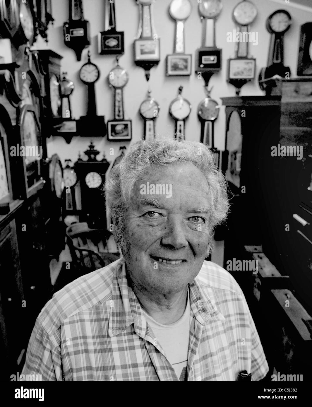 clock repair man stands infront of a wall of clocks Stock Photo