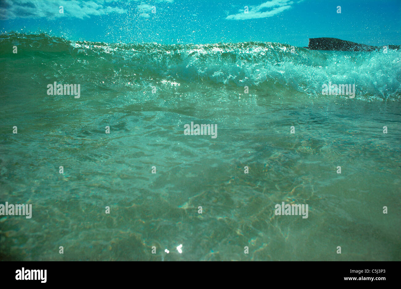 Semi-abstract image of a single green wave breaking towards the camera with a solitary distant headland just visible above the Stock Photo