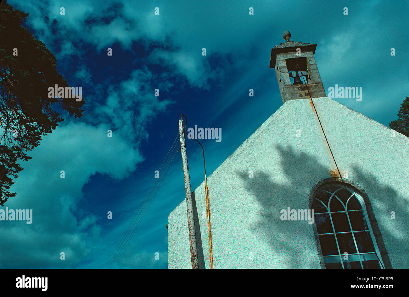 Semi-abstract image of white-wasked gable and belfry of small village church jutting at an angle up into a deep blue and cloudy Stock Photo