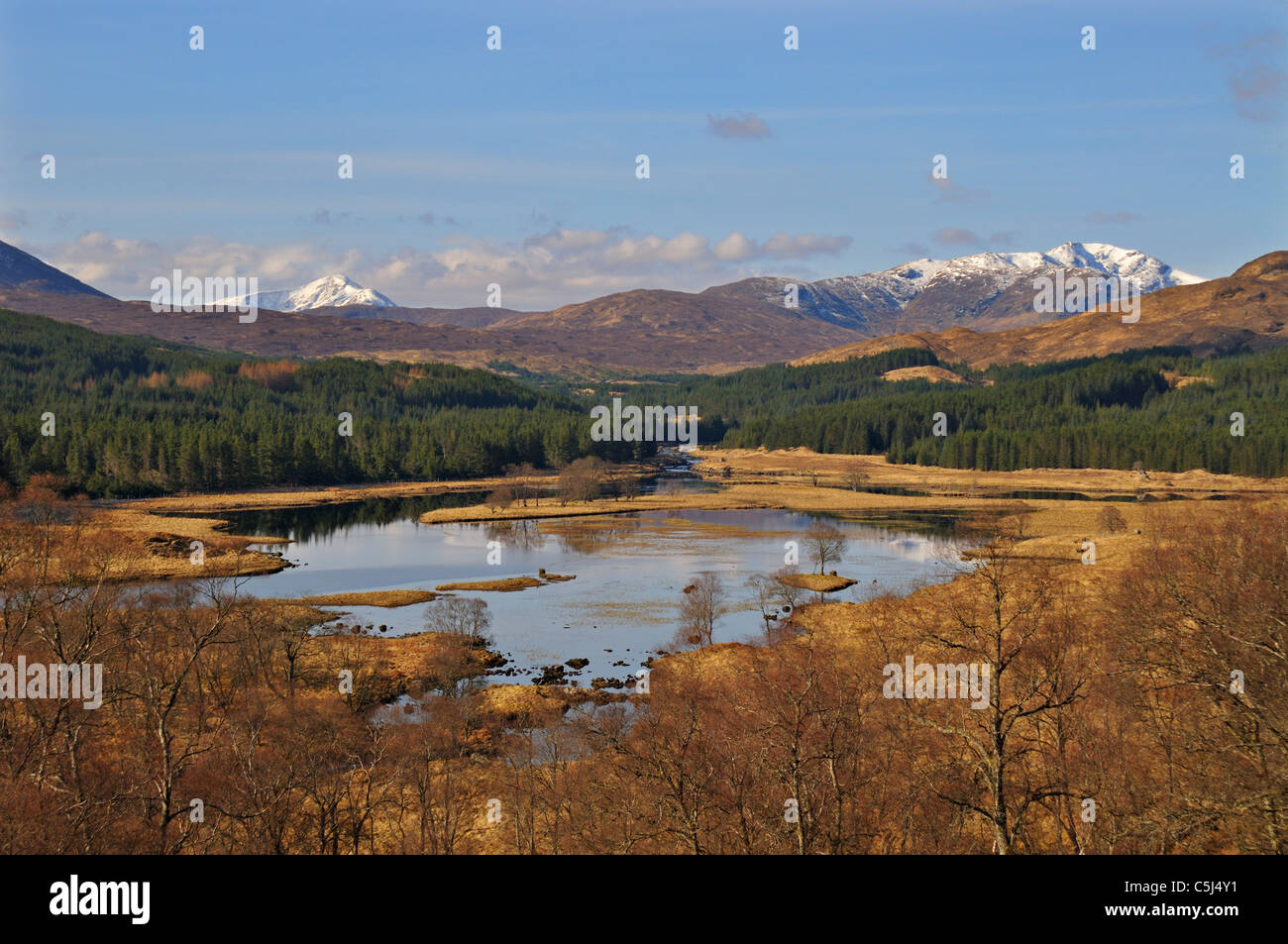The broad River Garry, flanked by trees and with hills and snow-capped mountains behind, Glen Garry, western Scotland, UK. Stock Photo