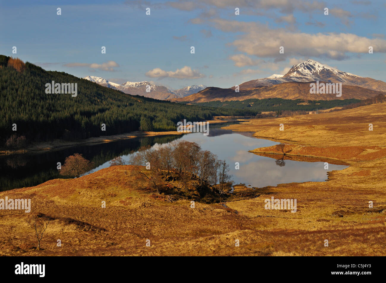 The broad River Garry, flanked by trees and with hills and snow-capped mountains behind, Glen Garry, western Scotland, UK. Stock Photo