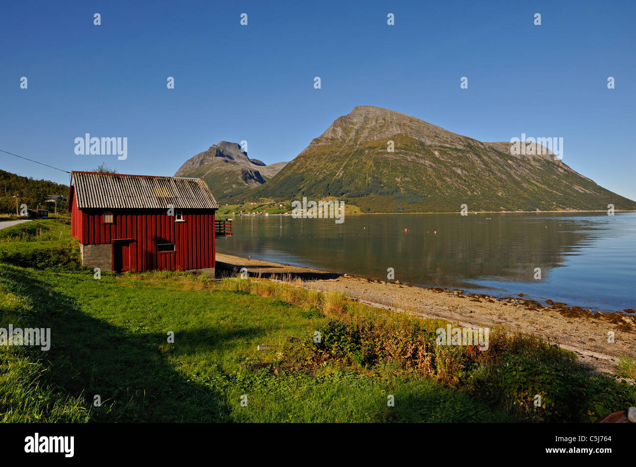 Red wooden boathouse at Lia with the island of Aldra and the Hjarttinden peaks behind, north-west Norway. Stock Photo