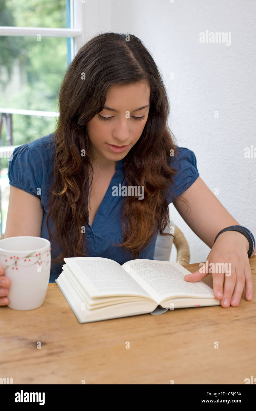 Young woman sat at table reading a book Stock Photo - Alamy