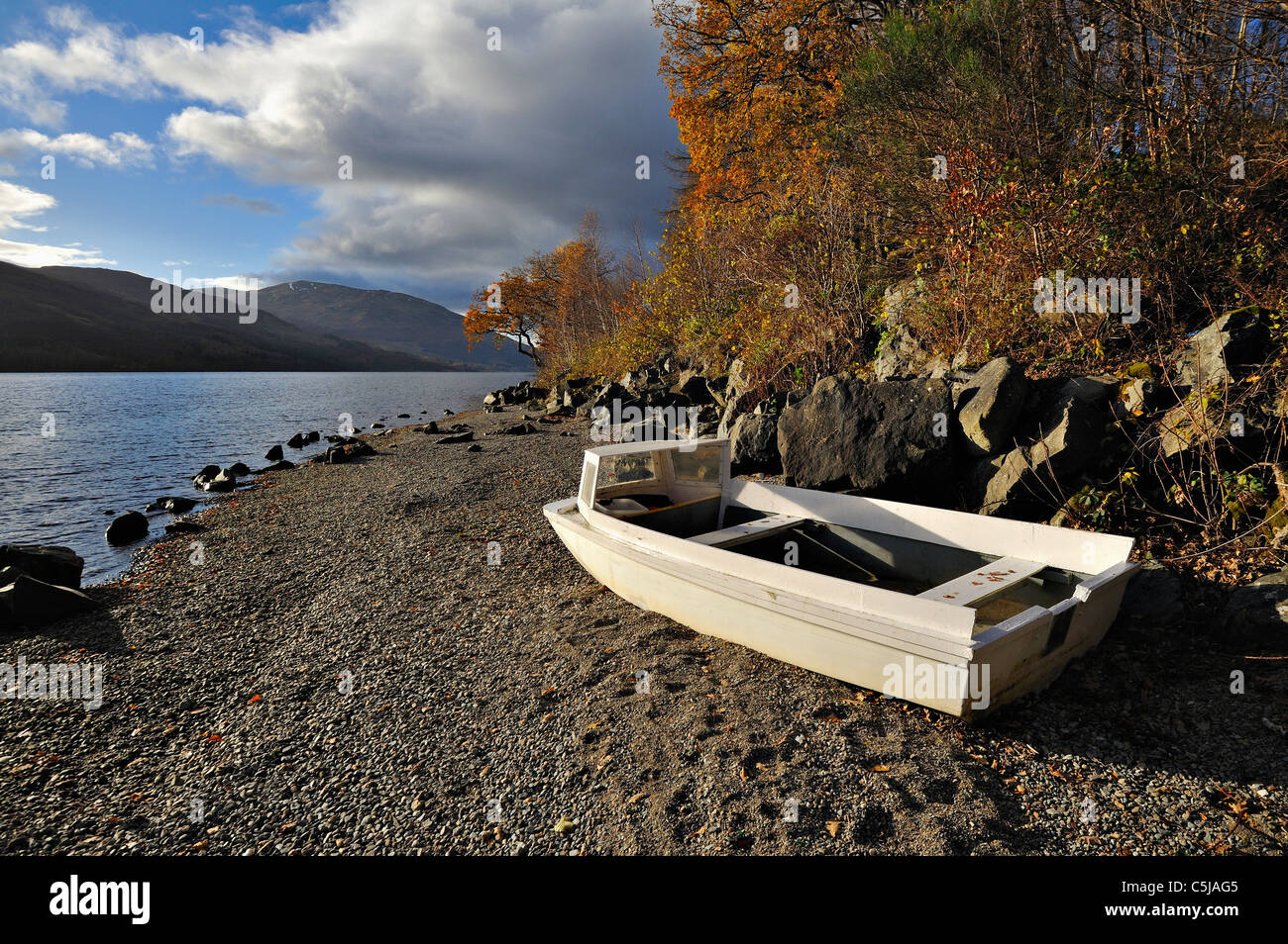 Abandoned boat on a rocky shoreline under autumn trees, Loch Earn, Perthshire, Scotland Stock Photo