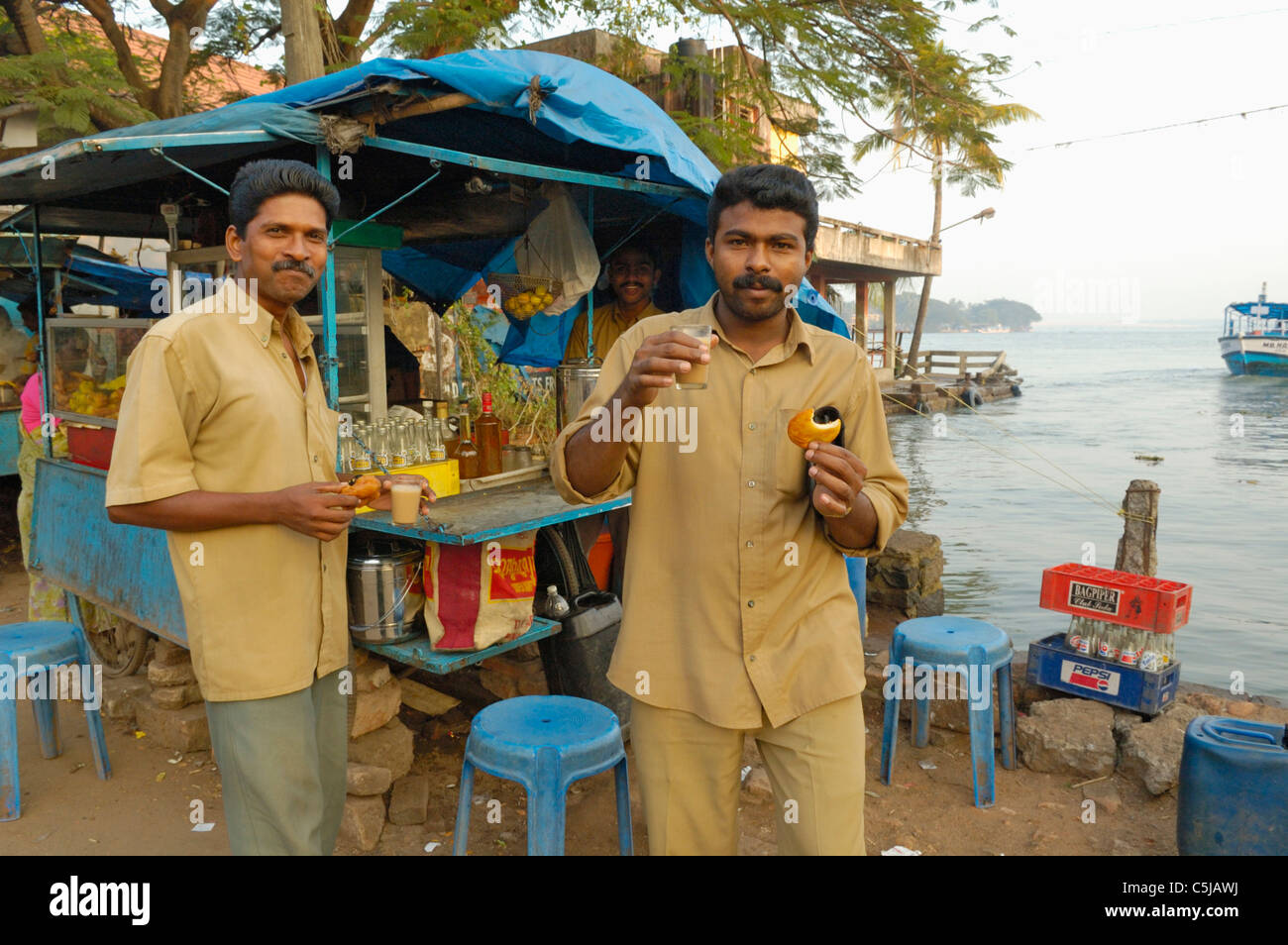 Two indan man in the harbour of Fort Cochin having a sweet tea and biscuit at one of the typical small mobile tea shops, Fort Stock Photo