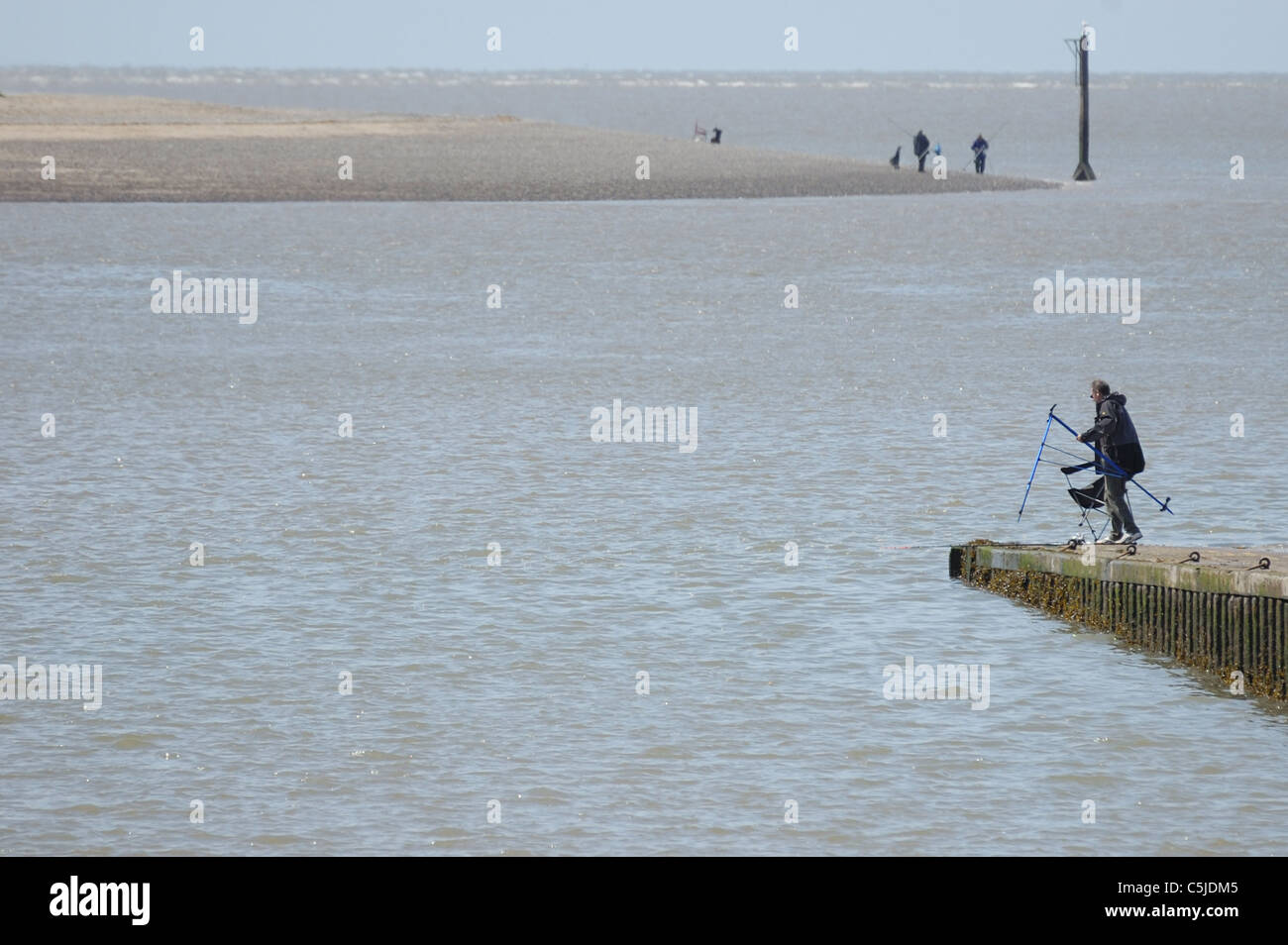 An angler setting up equipment at end of stone jetty slipway Stock Photo