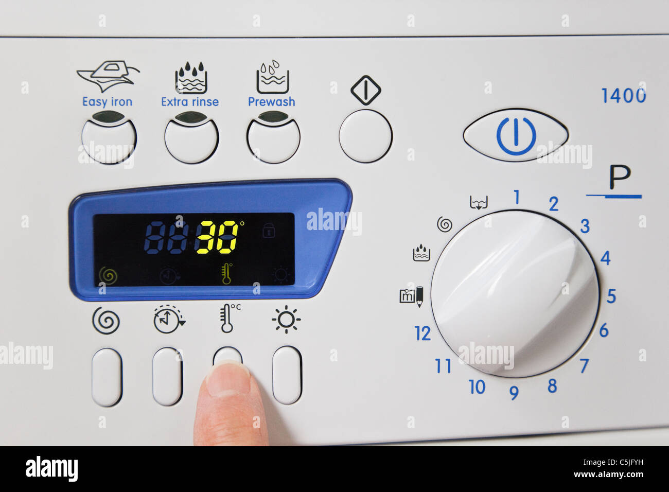 Person setting an automatic washing machine on an easy care program at a low temperature cool wash of 30 degrees to save power Stock Photo