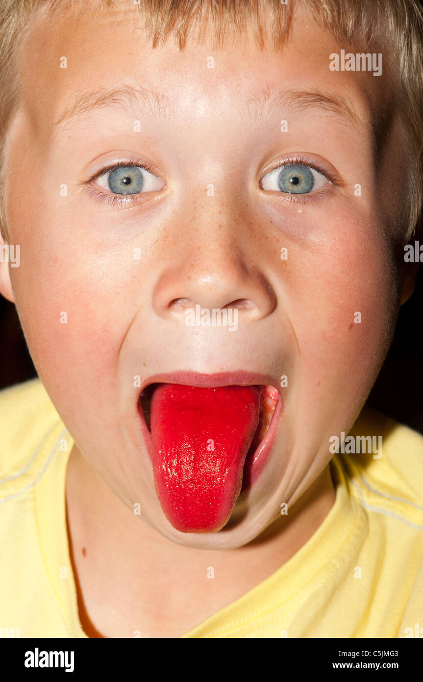 A seven year old boy shows his red tongue after drinking a ...