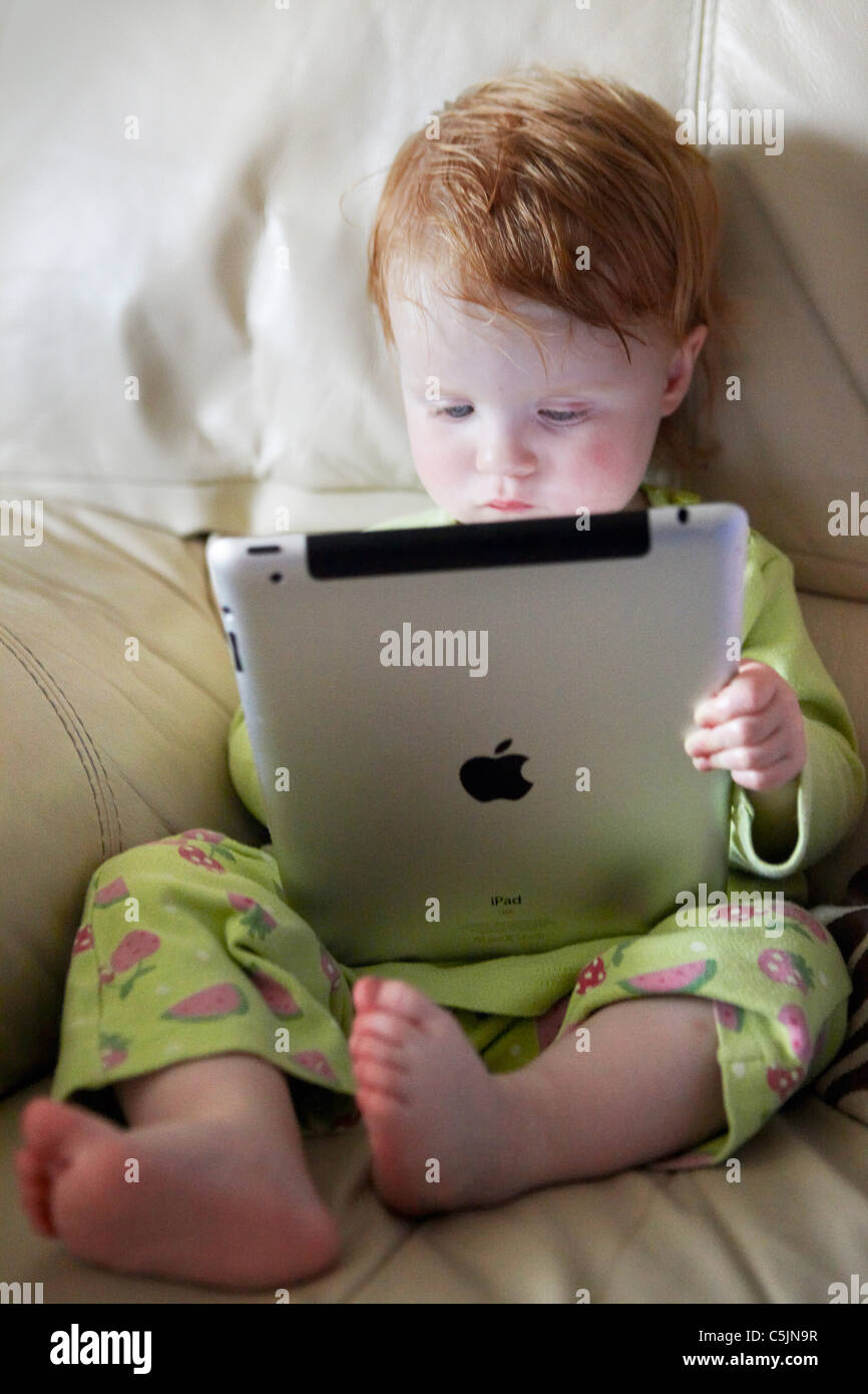 2 year old Baby girl playing with her  iPad2 on the sofa Stock Photo