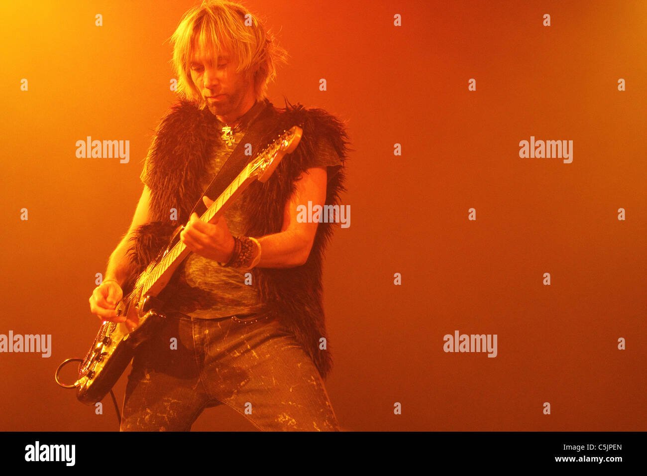 The lead guitar player of a rock and roll band performs on stage with red and yellow lights Stock Photo