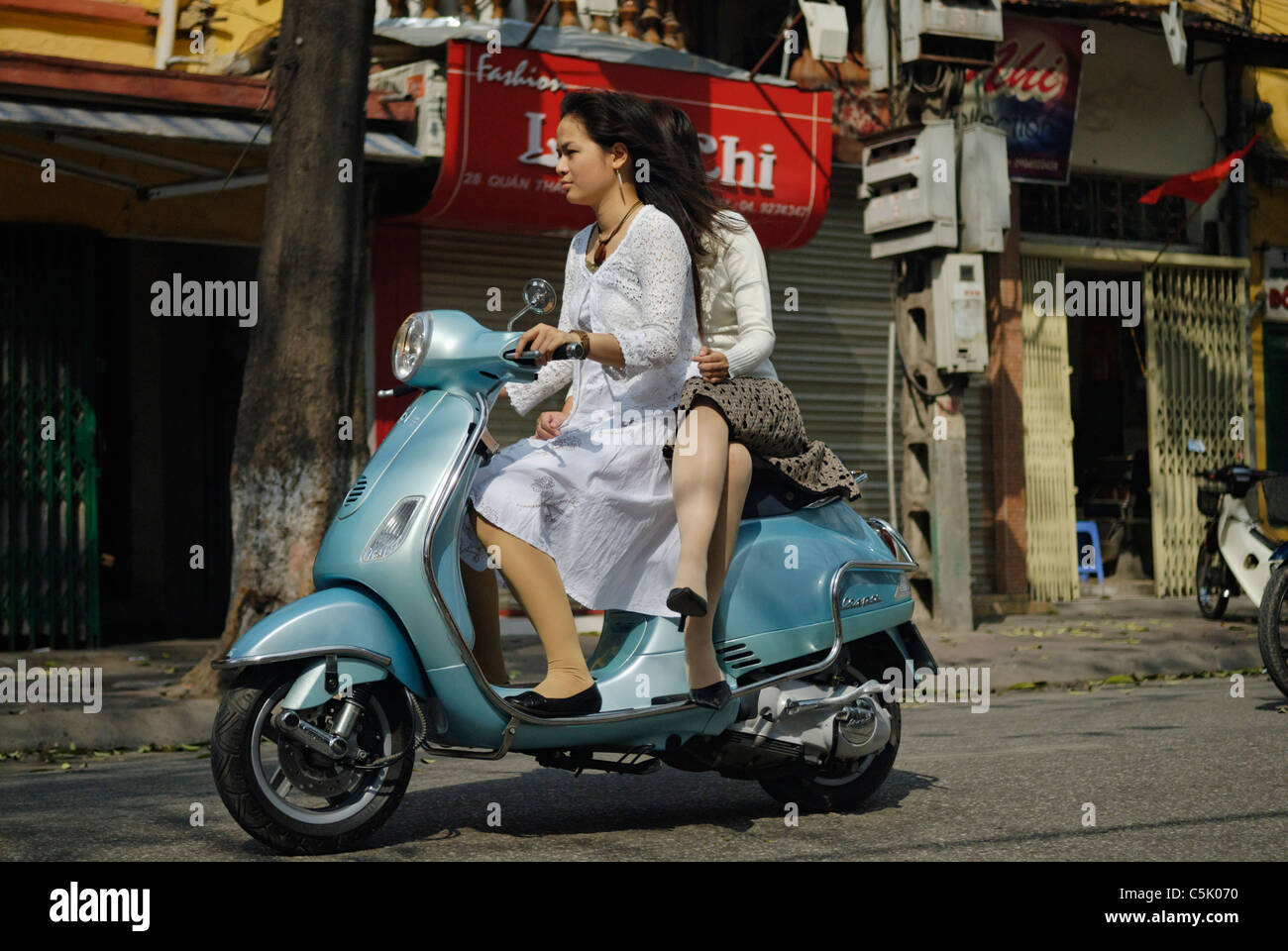 Asia, Vietnam, Hanoi. Hanoi old quarter. Two young dressy vietnamese women riding a Vespa motorbike through Hanoi. Stock Photo