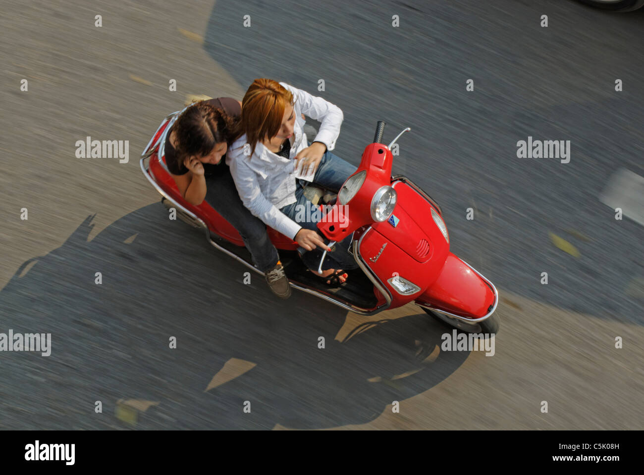 Asia, Vietnam, Hanoi. Hanoi old quarter. Young fashionable vietnamese women riding a red Vespa motorbike through Hanoi. Stock Photo
