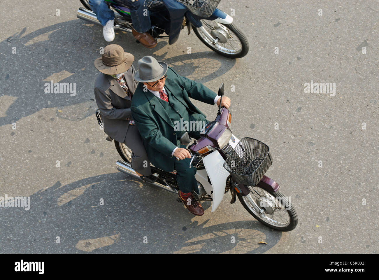 Asia, Vietnam, Hanoi. Hanoi old quarter. Elderly vietnamese couple, wearing suit and hat, riding on a small motorbike through Stock Photo